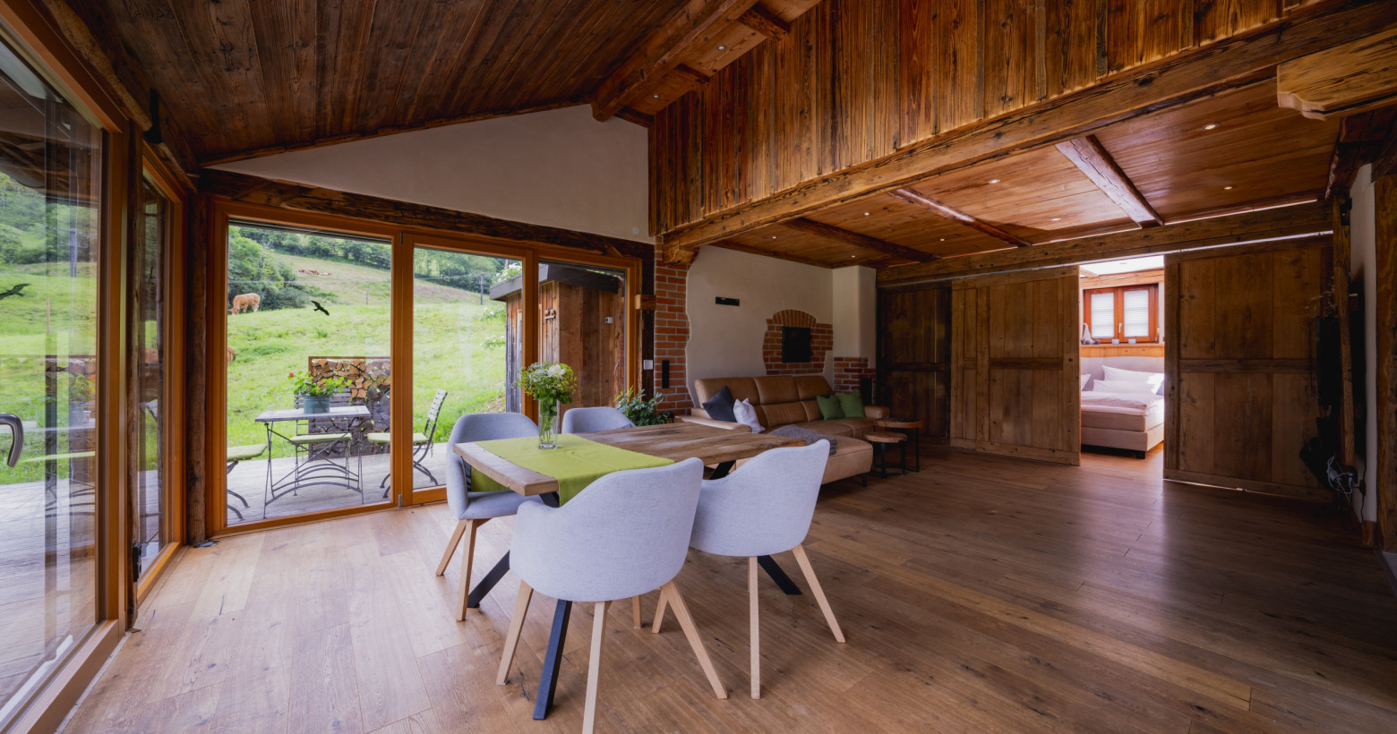 Blick in die Ferienwohnung Alte Backstube mit Esszimmertisch, Couch und Wintergarten. Rechts hinten sieht man hinter der Schiebetür das Boxspringbett.