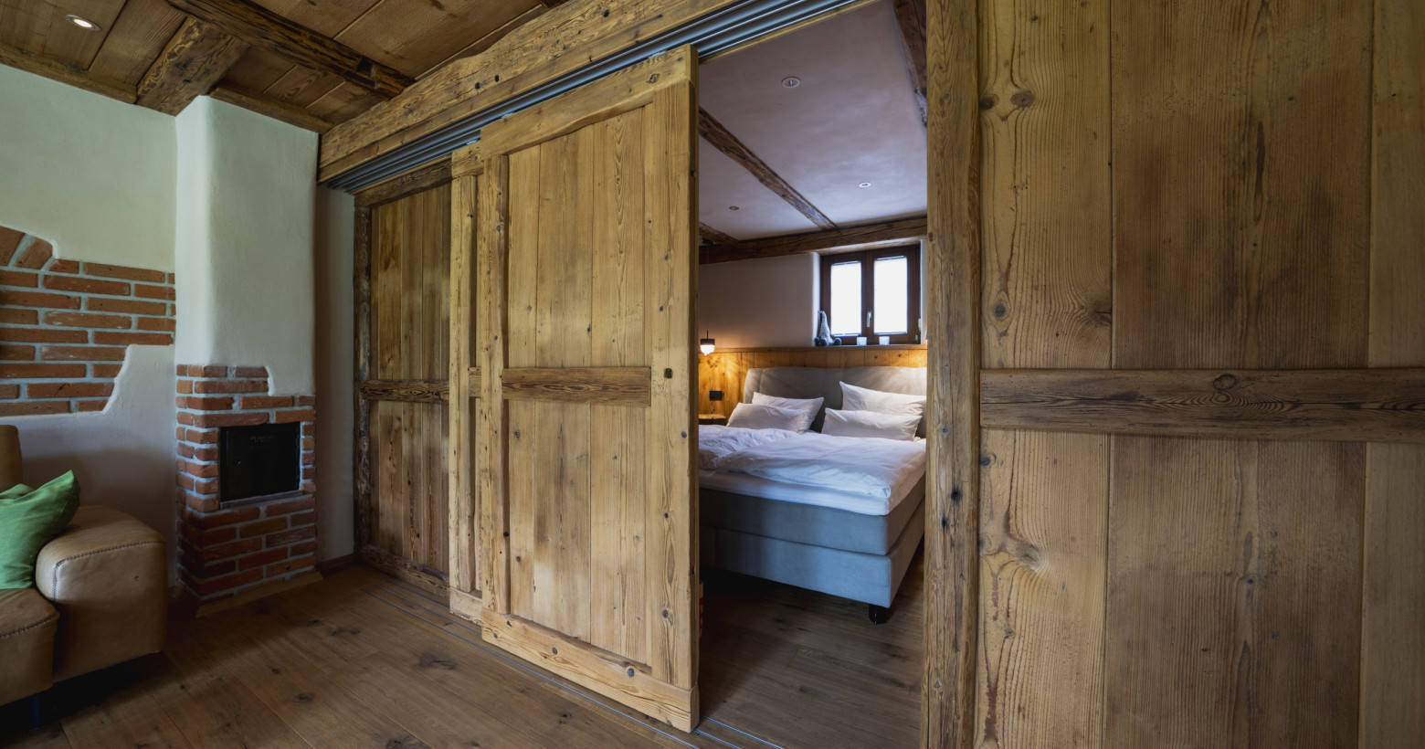 Blick in den Schlafbereich der Ferienwohnung Alte Backstube. Hinter der rustikalen Holz-Schiebetür sieht man das Boxspringbett. 